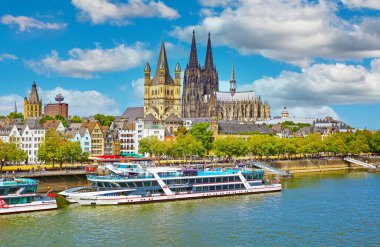 Cologne, Germany - July 9. 2022: Riverside skyline with dome, roman Saint Martin church, TV tower, rhine river cruise ships, blue summer sky, fluffy clouds