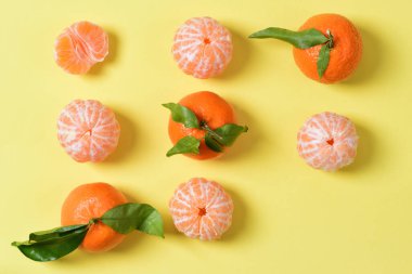 Birkaç mandalina yan yana, soyulmuş ve soyulmamış olarak yatar, bir mandalina ise sadece yarısıdır. Bazı meyvelerin yeşil yaprakları vardır. Bir parça eksik.