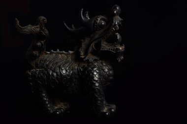 Dark close-up of an old Chinese dragon figure made of wood, which stands in front of a dark background and already shows some signs of wear
