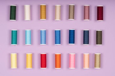 Renkli dikiş ipliklerinin farklı renklerdeki makaralarının üst çekiminde. Pembe arka planda yan yana yatıyorlar..