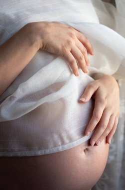Karnında şişkinlik olan hamile bir kadının karnına yakın çekim ve detaylı çekim. Karnı hassas bir kumaşla kaplı.