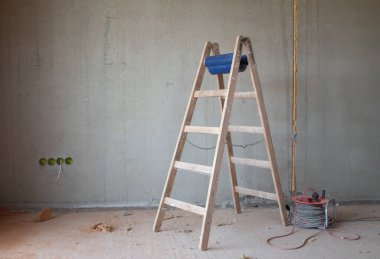 Bir evin kabuğunda, gri beton bir duvarın önünde, eski bir ahşap merdiven var. Odada, yerde çok fazla toz var. Kenarında bir kablo varili var..