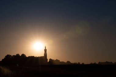 Sunset behind a catholic church in Bavaria. The sky is blue and red. You can see the rays of the sun. There is space for text.