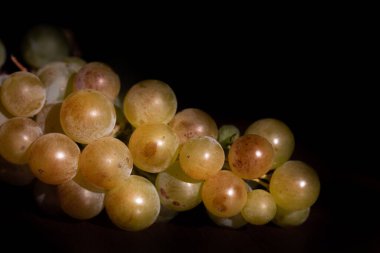Sweet ripe grapes lie on a table against a dark background
