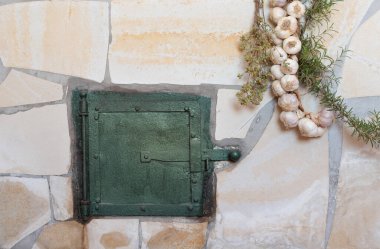 Background and closeup of a traditional oven with an oven door. Herbs and garlic hang down on the sides