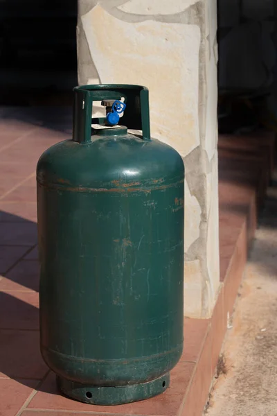 A green metal gas bottle stands on a terrace in Italy. It is a deposit bottle that should be refilled