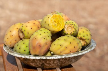 Several ripe prickly pear fruits lie in a ceramic bowl. The bowl stands on a base made of rustic wood.
