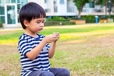 Asyalı küçük çocuk çimenlerde tek başına oturuyor..