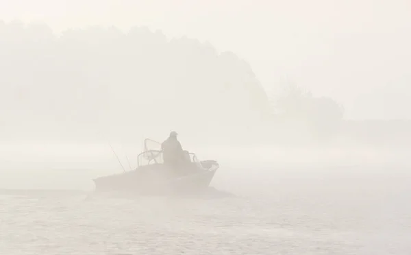 Pescador solitário em um barco, nevoeiro pesado no lago — Fotografia de Stock