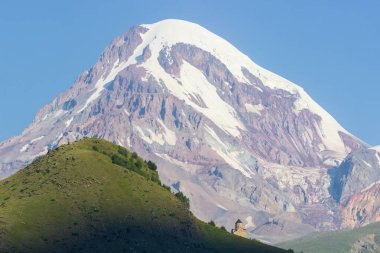 Gürcistan, Stepansminda 'daki Gergeti Trinity Kilisesi' ne uzaktan bakış. Arkadaki Kazbegi Dağı 'nın üstündeki açık gökyüzü. Gün doğumu, gün batımı