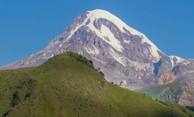 Gürcistan, Stepansminda 'daki Gergeti Trinity Kilisesi' ne uzaktan bakış. Arkadaki Kazbegi Dağı 'nın üstündeki açık gökyüzü. Gün doğumu, gün batımı