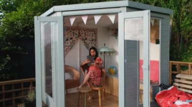 Bahçe yazlığında oturmuş tablet okuyan Asyalı genç bir kadın.