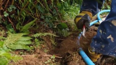 Plastik boru döşemek için elinde malayla bahçede çukur kazan bir adam.
