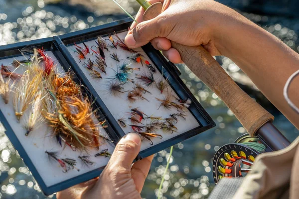 A close up of an asian female selecting fly fishing flies from a box