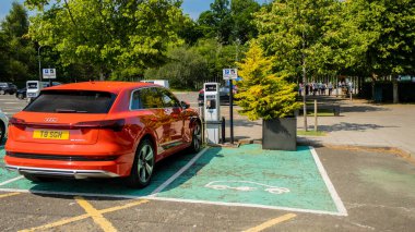Loch Lomond, İskoçya - 25 Temmuz 2021: Kırmızı Audi e-tron elektrikli araç bir otoparktaki bir istasyonda şarj ediliyor