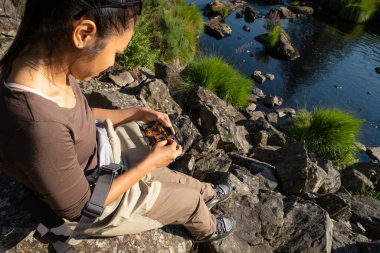 Asyalı bir dişinin sineği seçtiği yakın plan bir nehir kenarındaki kayalarda otururken, kutudan balık avlayan sinekler.