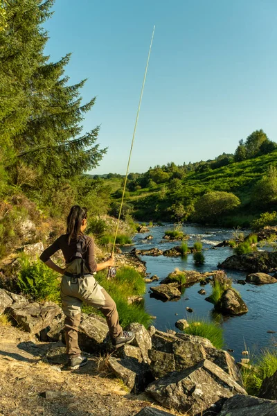 An asian female fly fisher women wearing waders and holding a rod, looking where to fish on a river