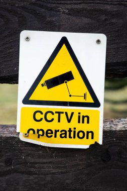 Ahşap bir çitin üzerindeki sarı güvenlik kamerası uyarı işareti kırılmış.