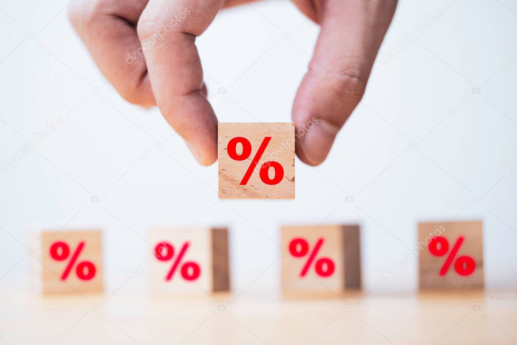 Hand holding red percentage symbol which print screen on wooden cube block for debt  interest rate and shopping discount concept.