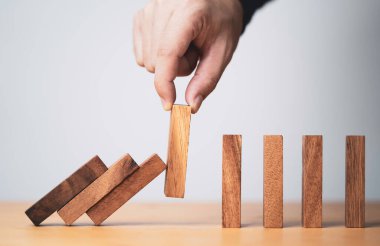 Domino taşının düşmesini önlemek ve engellemek için tahta bloğu elle sökmek, kriz yönetimi kavramının zarar görmemesi ya da zarar görmemesi için bir semboldür..