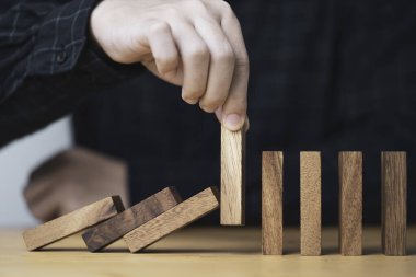 Domino taşının düşmesini önlemek ve engellemek için tahta bloğu elle sökmek, kriz yönetimi kavramının zarar görmemesi ya da zarar görmemesi için bir semboldür..