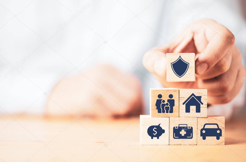 Businessman putting wooden cube block stacking with insurance and assurance icon including family health real estate car and financial for risk management concept.