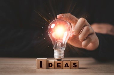 İş adamı, yaratıcı fikir ve yenilik kavramı için fikirlerin yazılı olduğu ekranda parlayan ampule dokunuyor..