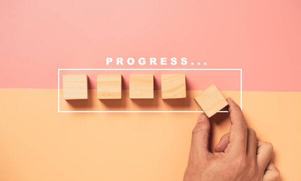 Hand putting wooden cube block on half of pink and orange background with graphic loading for project job progressive concept.