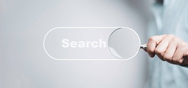 Arama motoru optimizasyonu veya SEO konsepti için arama çubuğu simgesiyle el ele tutuşan büyüteç.