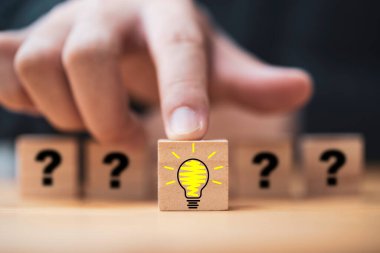 Hand pushing lightbulb drawing which print screen on wooden cube block among human and question mark for creative thinking idea and problem solving concept.