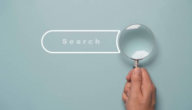 Hand holding magnifier glass with search bar icon for SEO or Search Engine Optimisation wording concept.