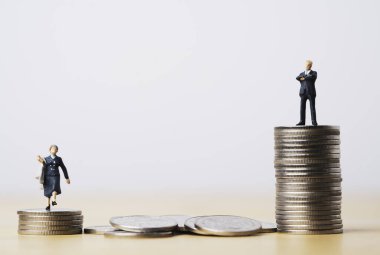 En yüksek sikkelerin üzerinde duran işadamının minyatür figürü ve şirket kavramında cinsiyet eşitsizliği için istiflenen en düşük sikkelerin üzerinde duran iş kadını.