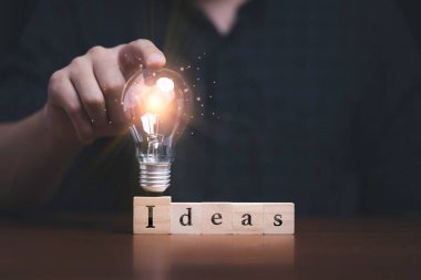 Yaratıcı düşünce ve problem çözme kavramı için ahşap küp bloğunda hangi ekranın yazılacağını belirleyen fikirler üzerine parlayan ampullere el dokunmak