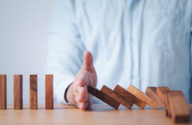 İşadamı elle durdurur tahta bloğu Diğerleri risk ve kriz yönetimi kavramına domino taşlarını engeller.