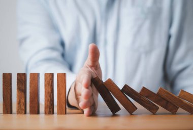 İşadamı elle durdurur tahta bloğu Diğerleri risk ve kriz yönetimi kavramına domino taşlarını engeller.