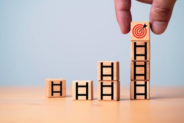 Hedef tahtasını merdivenin tepesine koyan el, iş hedefi ve amaç kavramının büyümesi için tahta küp bloğa ekran yazdıran el..