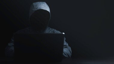 Siyah kapüşonlu bir adam bilgisayar güvenlik sistemindeki hackerların şifrelerini ve finansal teknoloji kötü yazılım konseptini açmak için bilgisayar laptopu kullanıyor..