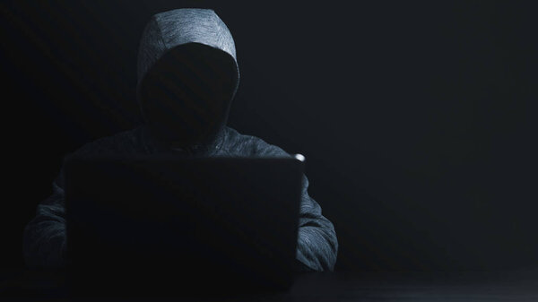 Man in black hoodie using computer laptop to unlock password for hacker in computer security system and financial technology malware concept.