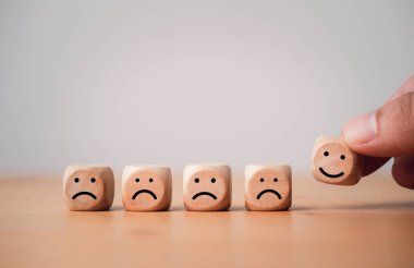 Hand holding smile face which print screen on wooden cube block among sad face for positive thinking mindset concept.