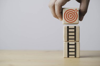 Hand holding red dartboard with arrow and ladder which print screen on wooden block for increasing of setup business objective target and goal concept.