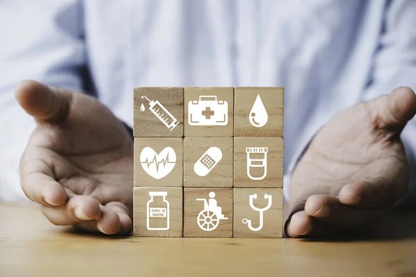 Businessman open the palm hand to present healthcare icons on wooden block cube for health insurance and life assurance concept.