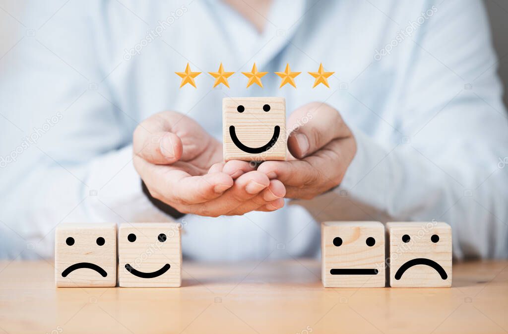 Businessman holding smile face on wooden cube block with other face emotion for excellent evaluation and customer satisfaction concept.