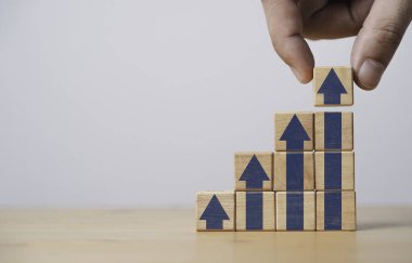 Hand stacking up arrow which print screen on wooden cube block for business investment ,financial interest  increasing rate and career path growth concept.