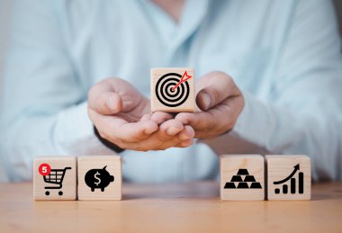 İş adamı hedef tahtası tutuyor. Bu tahtadan blokta ikonlarla birlikte baskı yapılıyor. Alışveriş arabası, domuzcuk tasarrufu, altın ve grafik ticari amaçlı yatırım hedefi kavramını oluşturmak için..