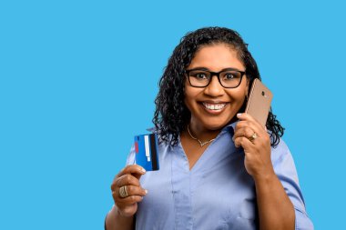 Kadın, elinde kredi kartı tutarken cep telefonuyla konuşur. İnternetten alışveriş yapar. Ödeme başvurusu yapar.