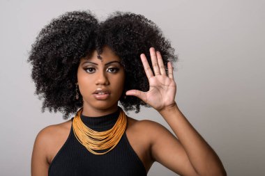 Siyah kadın portresi, gri arka planda izole bir şekilde el hareketini durdurur.