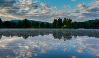 Dağlardaki gölette gün doğumu. Küstah Janowickie. Gökyüzündeki bulutlar. Bulutlar suya yansıyor. Ormanın etrafında. Arka planda dağlar. Suyun üzerinde sis