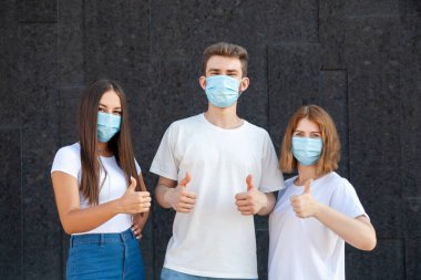 Jest, duygu, ifade ve insan konsepti - Beyaz tişörtlü beyaz adam ve iki kadın ve virüslerden korunan maskeler açık havada siyah arka planda fotokopi alanı ile başparmaklarını gösteren virüsler.
