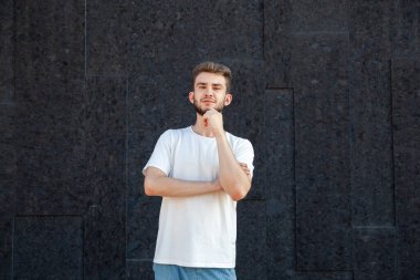 Duygular, jest, ifade ve insan konsepti beyaz tişörtlü ve kot pantolonlu düşünen beyaz sakallı bir adam bir elini yüzüne tutarak karanlık bir arkaplanda fotokopi çekmek istiyor.