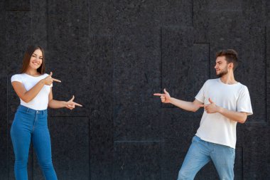 İfade, jest, duygular ve insan konsepti - Mutlu bir beyaz erkek ve kadın fotokopi alanının merkezine işaret ediyor ve siyah arka planda beyaz tişörtler ve mavi kot pantolonlar içinde duruyor 
